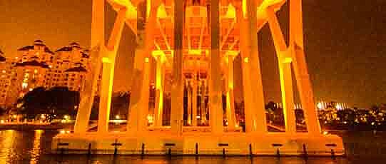 View from the water surface on orange lit pillars of a bridge.