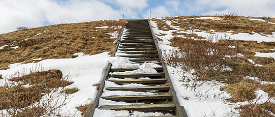 Stairs leading up to a partly snowy hill.