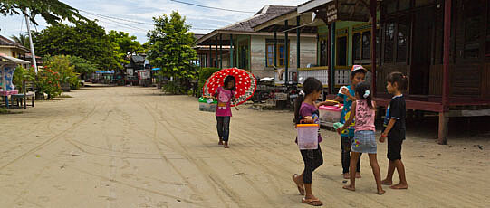 Sand path with palm trees, houses and children.