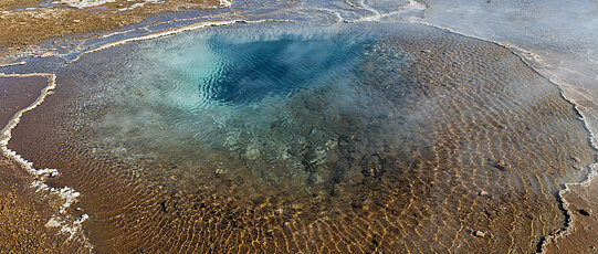 Tiefblaues, rundes Wasserloch mit zum Rand seichter werdendem Wasser.