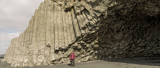 Man in a red jacket in front of columnar rock formations.