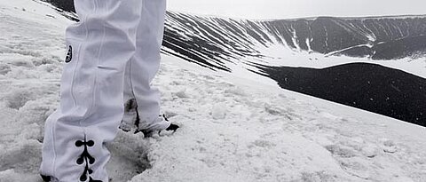 Hiker in white pants on snowy mountain with lake.