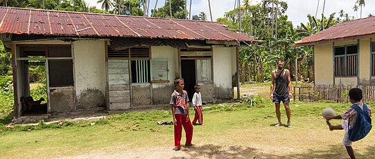 Children play football in front of two huts.