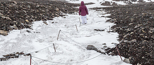 Wegmarkierung mit Wanderer auf verschneitem Berg.